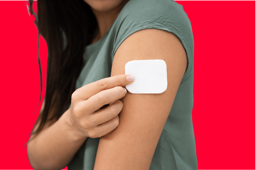 A cut-off image showing the upper torso of a woman who is placing a white patch on her upper arm. She is wearing a light green-colored shirt and the background of the image is red.